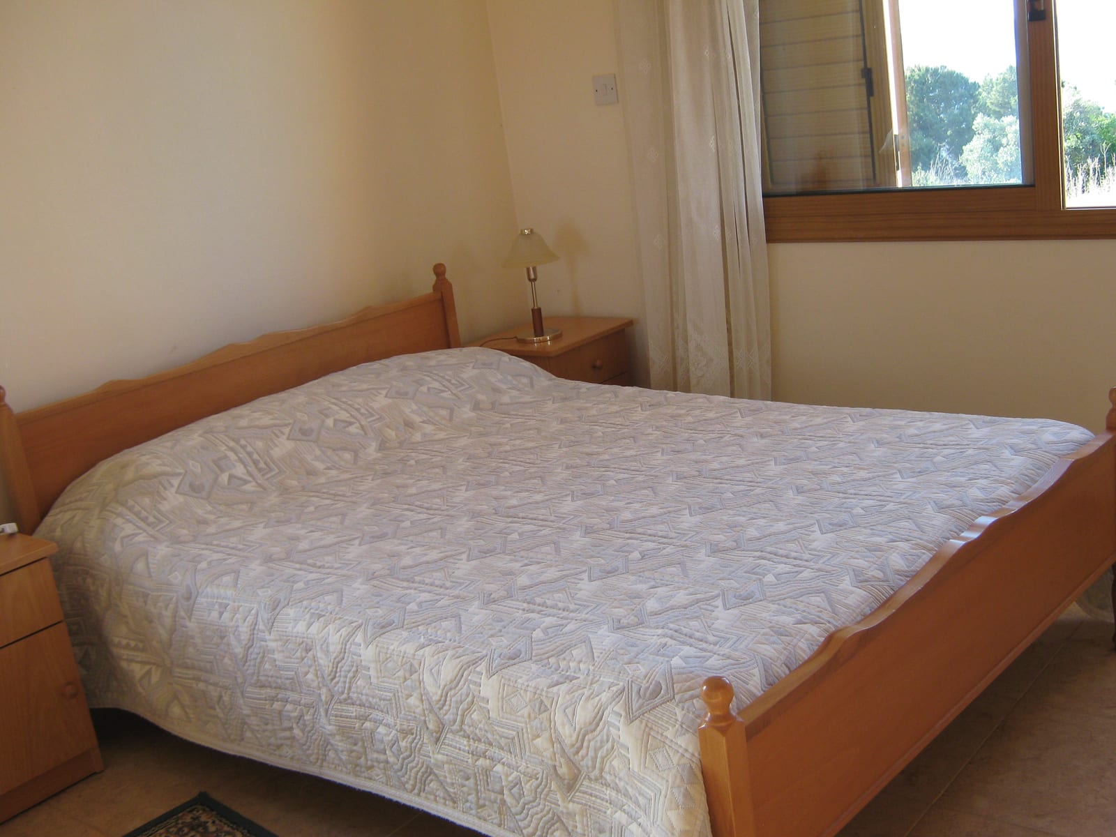Double bedroom with a wooden bed frame, bedside tables and a window onto the garden