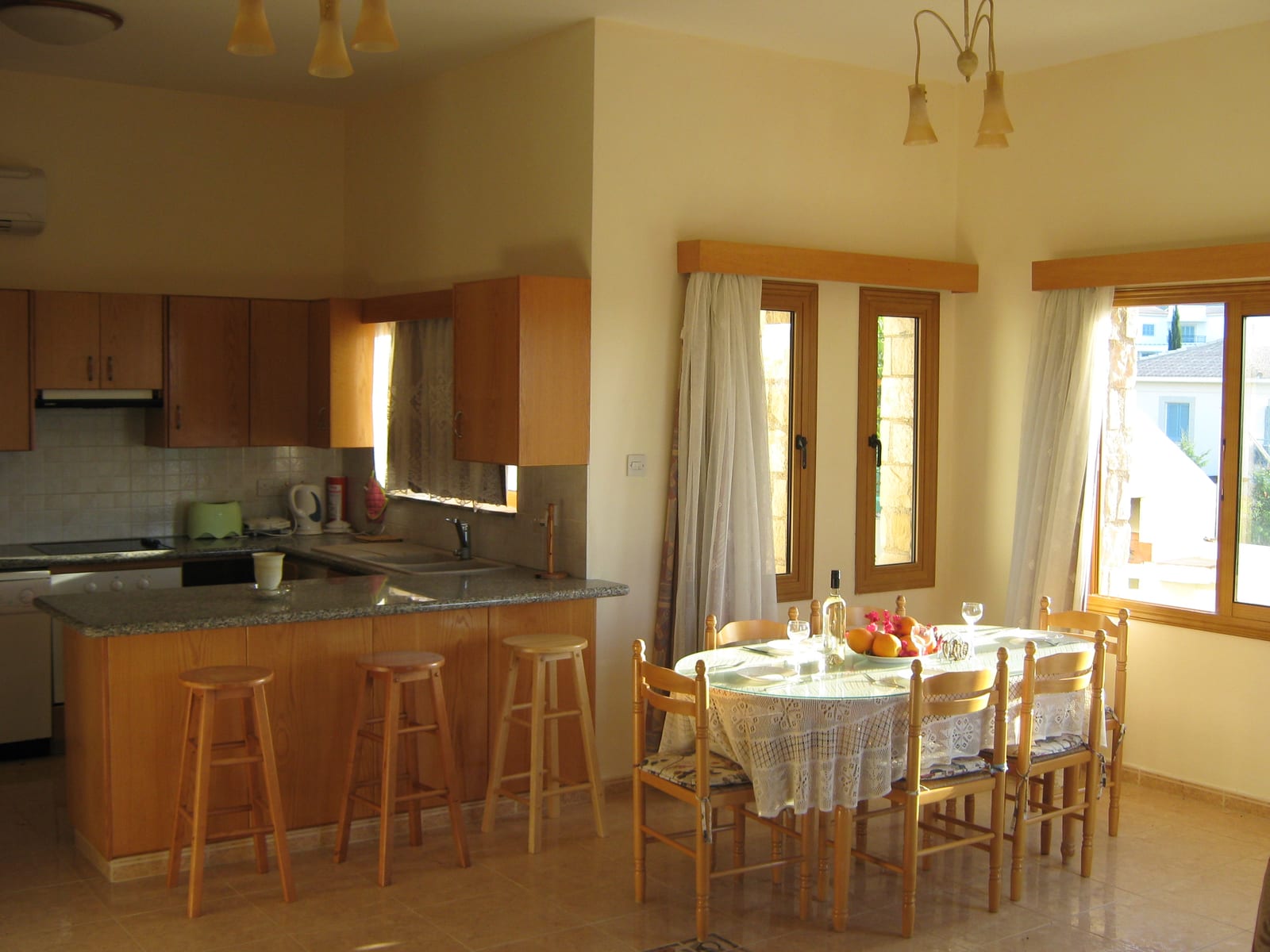 Open plan kitchen with a granite breakfast bar, bar stools and a dining table set for six