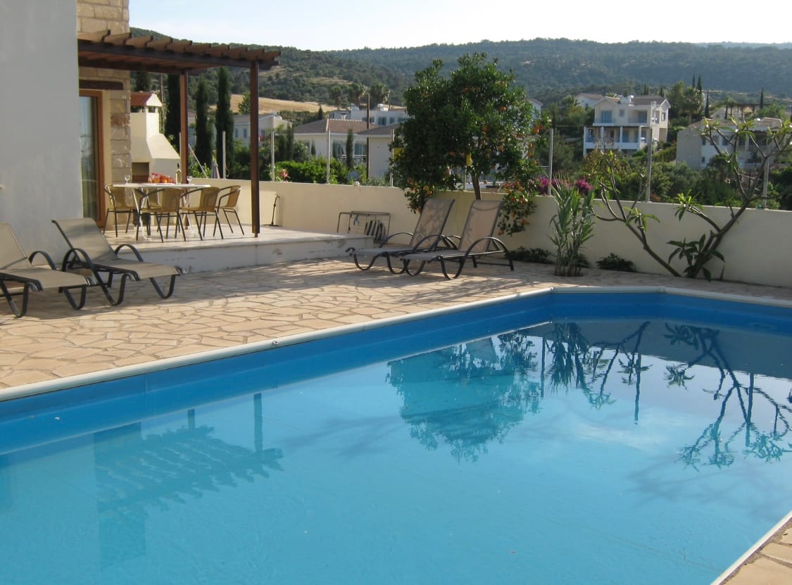 The nine metre swimming pool with sun loungers and the pergola shaded terrace behind it